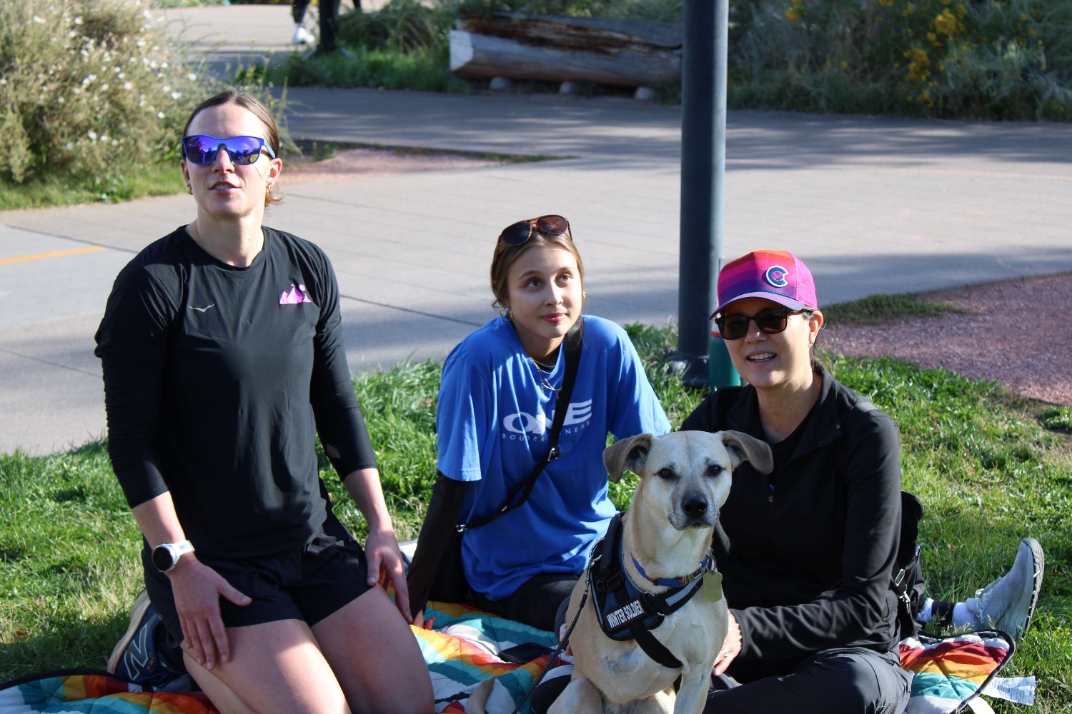 Three members sitting on the grass with a dog