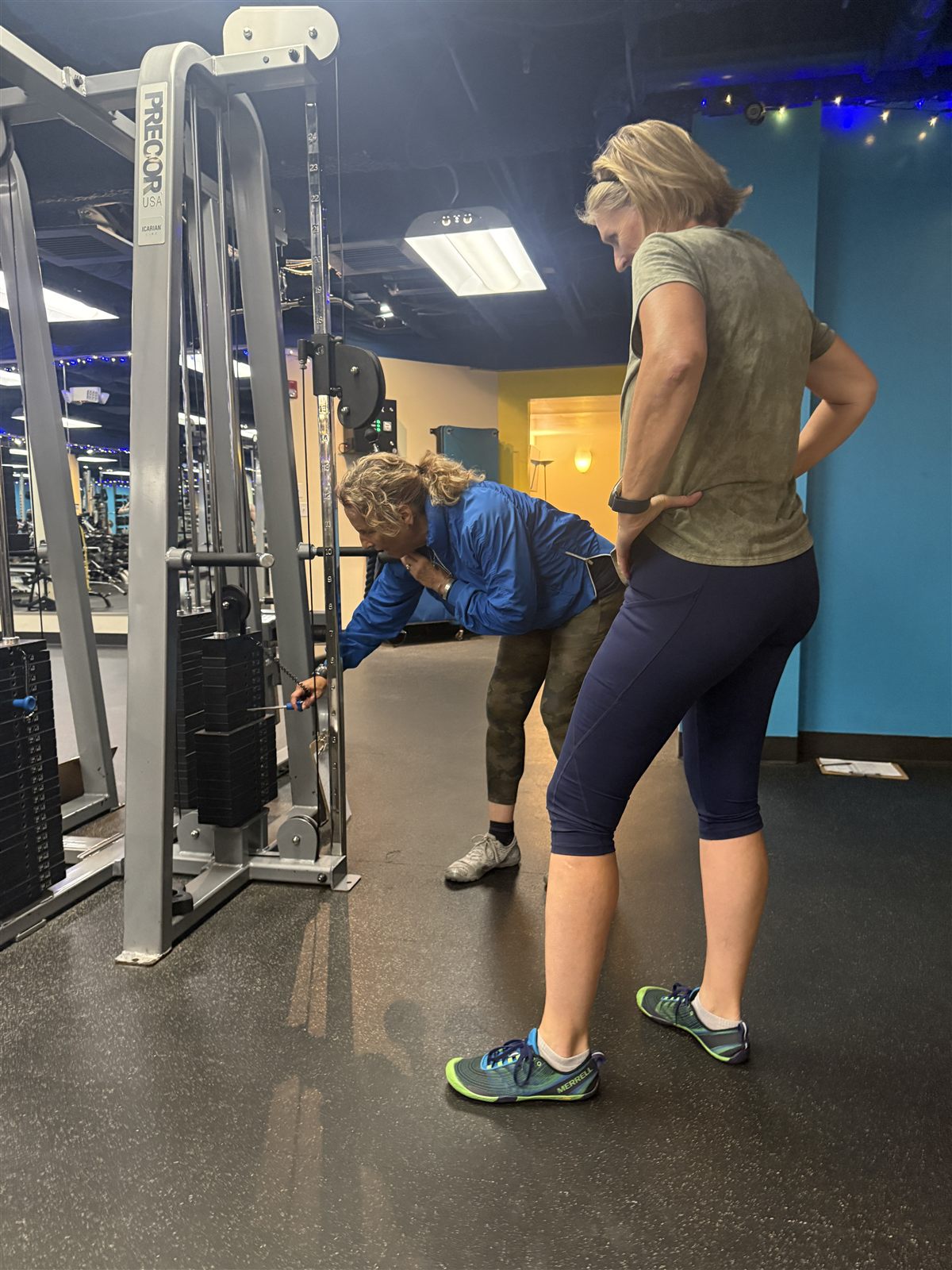 A trainer coaching a member's form on the cable machine at ONE Boulder Fitness